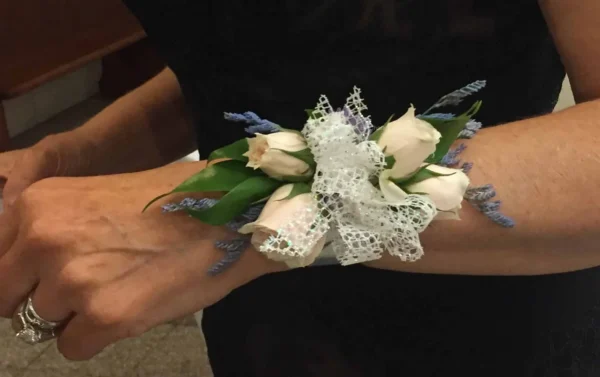 A person wearing a wrist corsage with white roses.