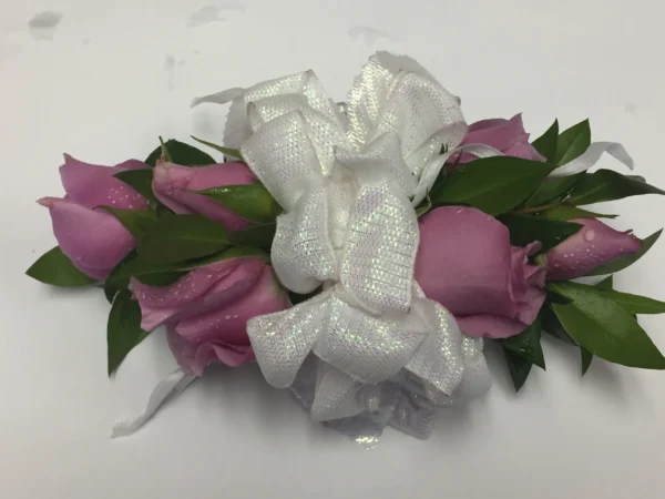 A white bow with three pink roses on top of it.