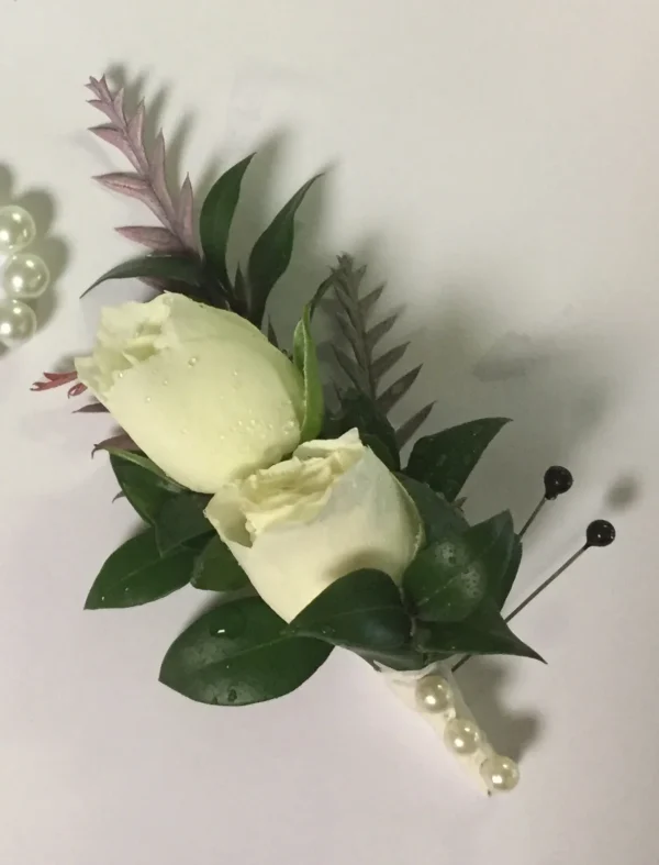 A white rose corsage with pearls and greenery.