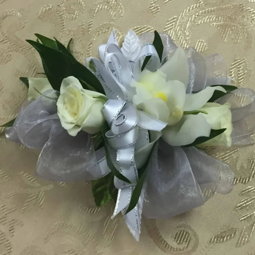 A white corsage with two roses and some leaves.