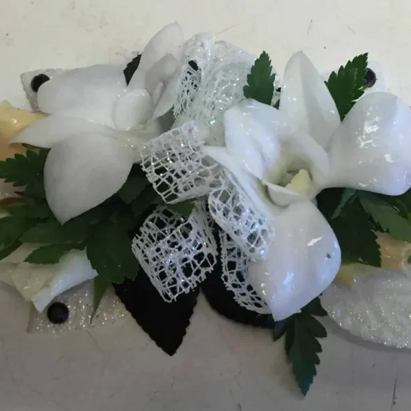 A white flower arrangement with green leaves and a bow.