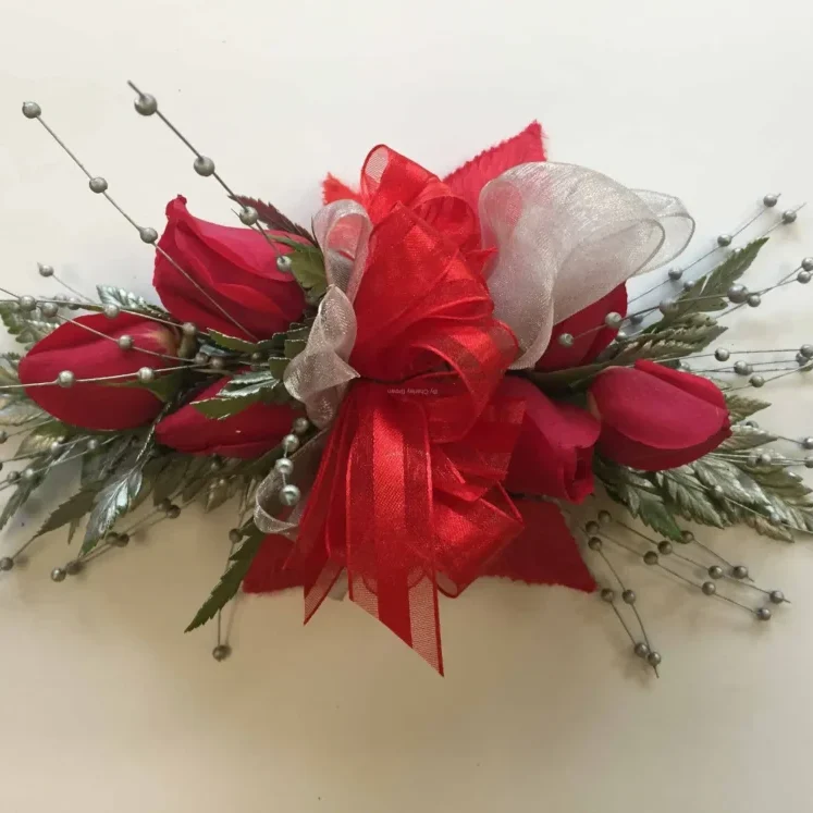 A red flower corsage with silver leaves and white ribbon.